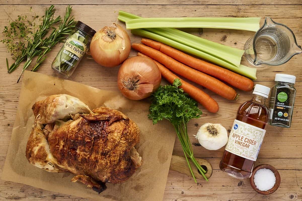Ingredients for rotisserie chicken stock including carrots, onions, celery, herbs, and chicken bones.