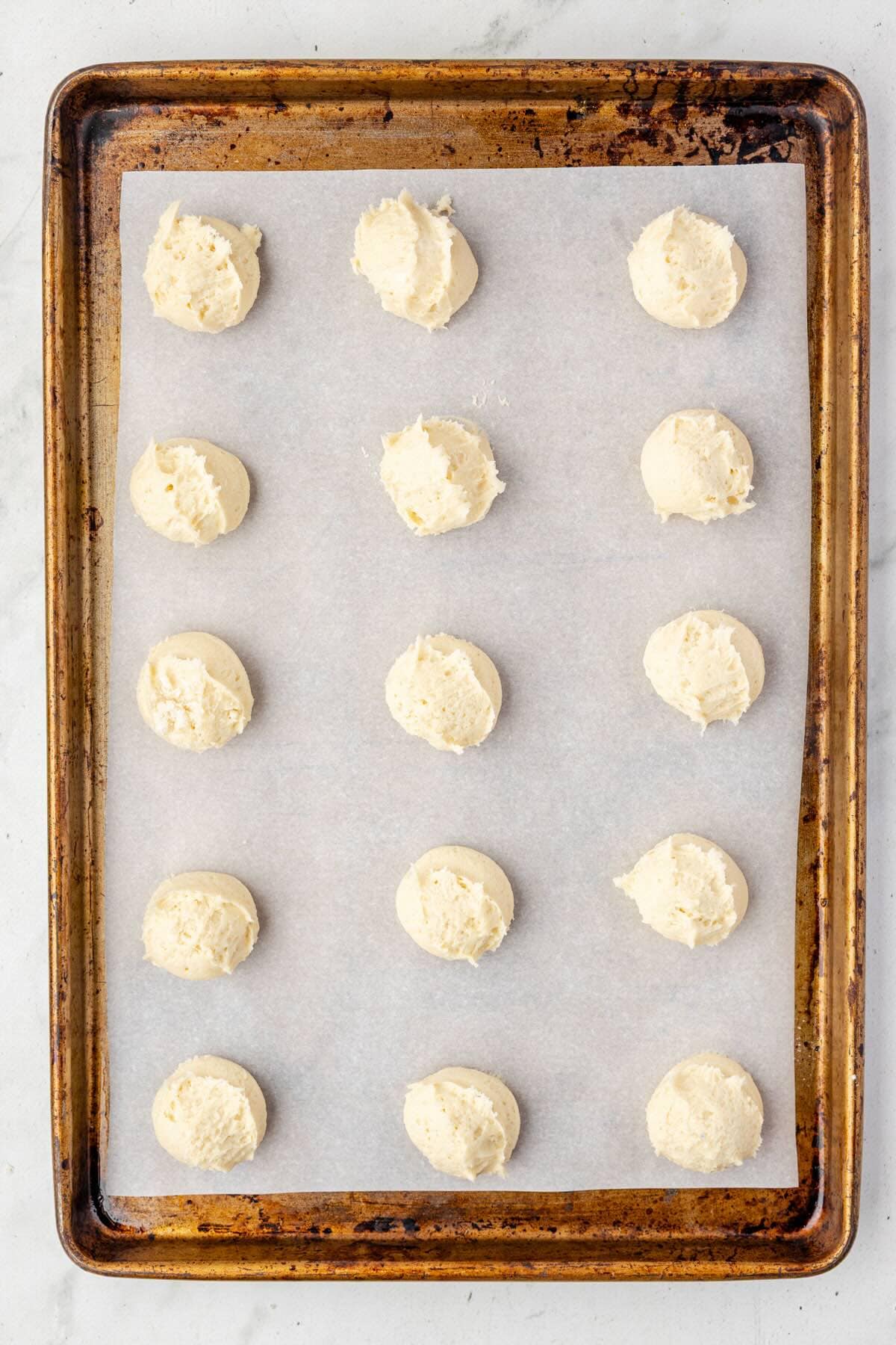 Scooped heaping tablespoons of cream cheese cookie dough onto a parchment-lined baking sheet.