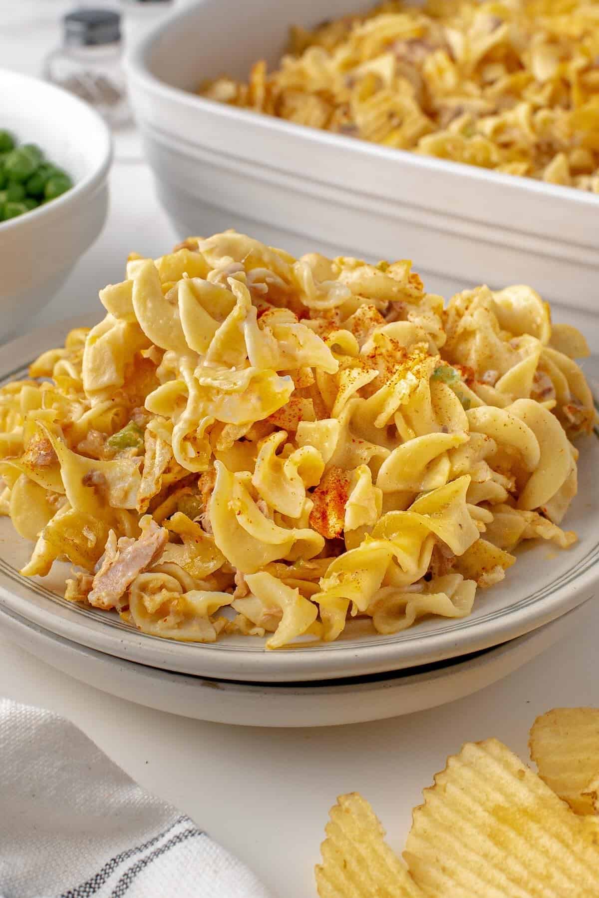 A serving of creamy tuna noodle casserole on a plate with peas.