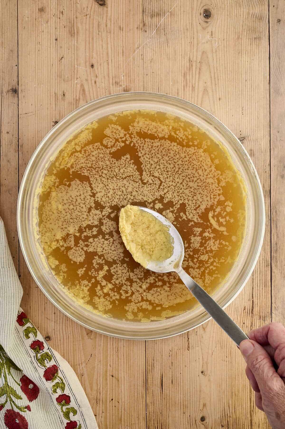 Using a spoon to skim the fat from chicken stock.