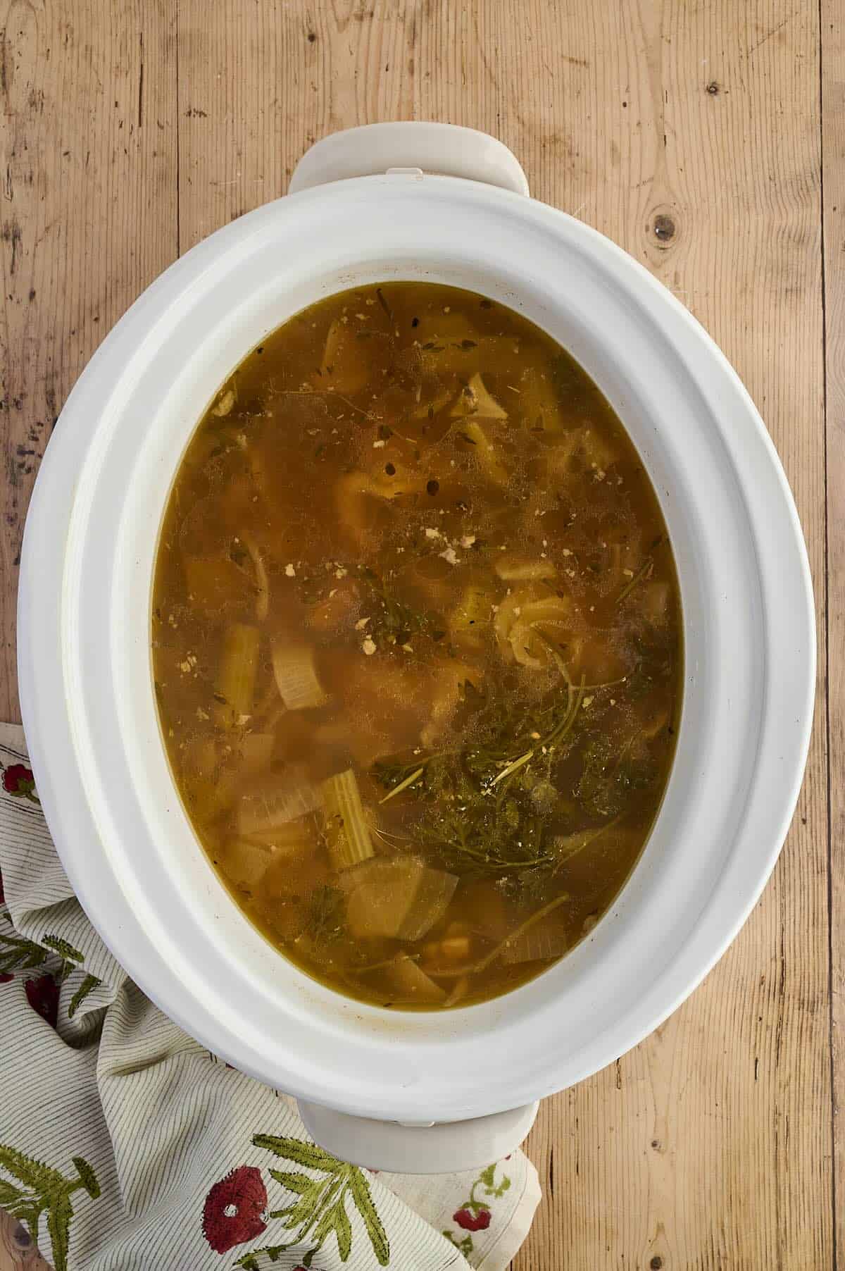 Slow cooker full of simmering chicken bones, veggies, and herbs for bone broth.