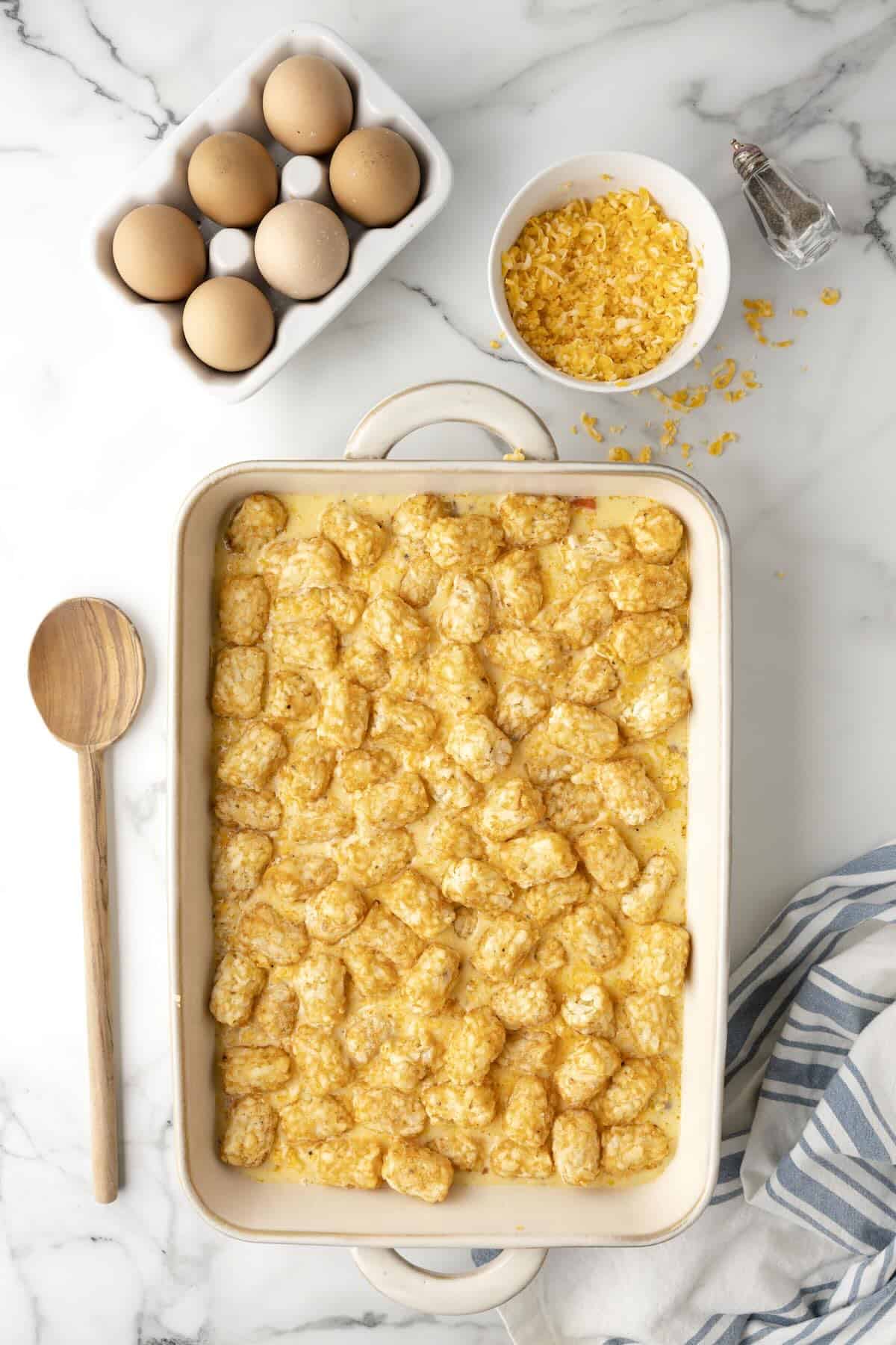 Unbaked egg casserole with tater tots on top in white baking dish before going into oven.