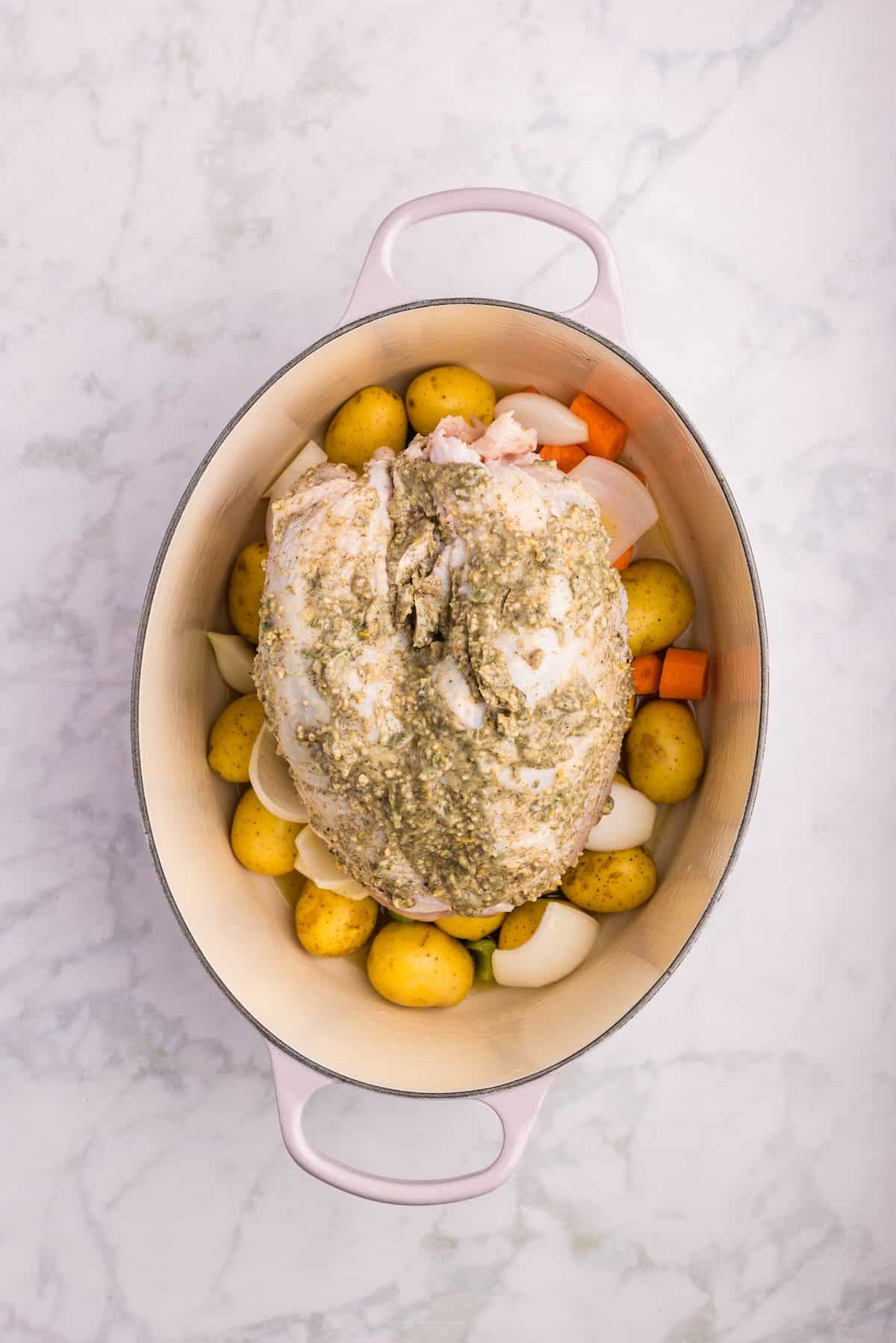 Bone-in turkey breast rubbed with herb butter and placed on top of seasoned vegetables in a roasting pan before going into the oven.