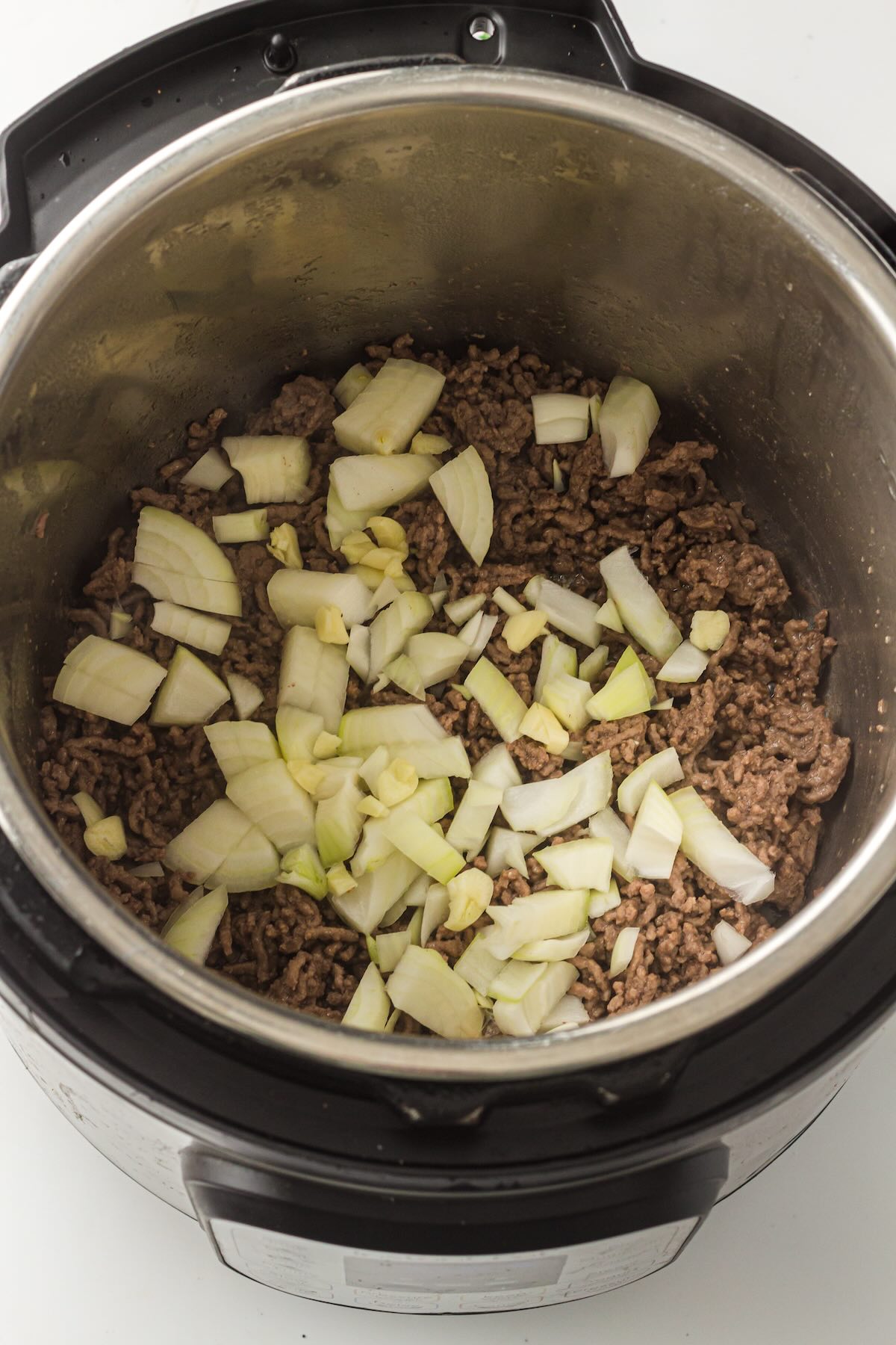 Diced onion and minced garlic added to browned ground beef in the Instant Pot for extra flavor.