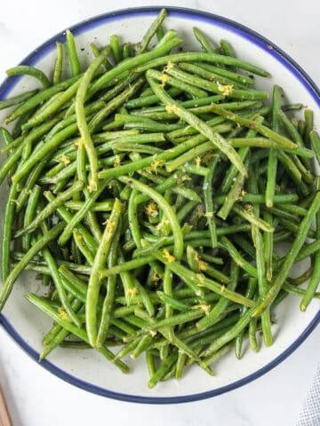 A bowl of cooked green beans fresh from the air fryer, garnished with lemon zest.