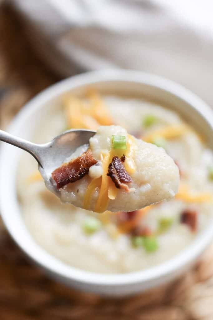 Spoon lifting a bite of creamy potato bacon soup with melted cheese and bacon.