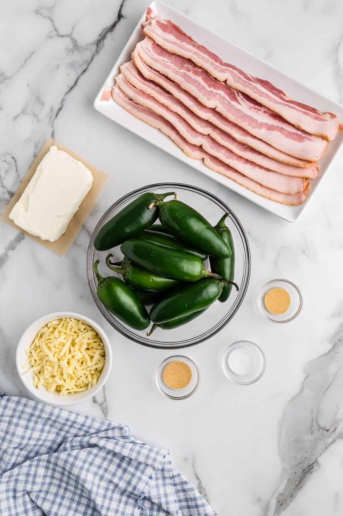 Ingredients to stuff jalapeno halves with shredded cheese, cream cheese, spices and bacon for wrapping.