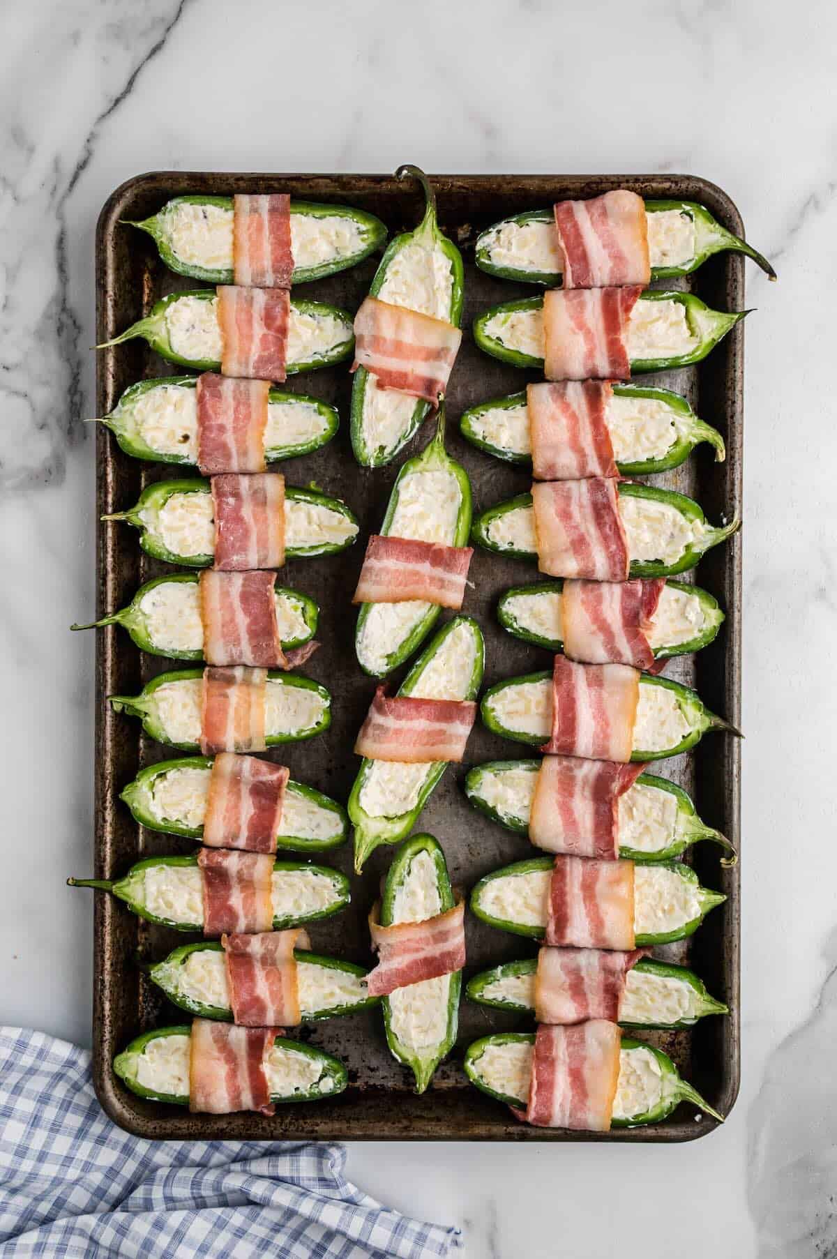 Bacon-wrapped jalapeño poppers arranged on a baking sheet ready for the oven.