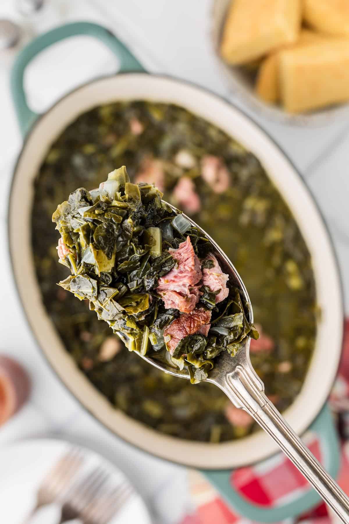 Collard greens being lifted with a spoon showing tender greens and smoky ham.