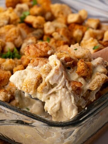 A spoonful of chicken, stuffing and gravy in a casserole dish.