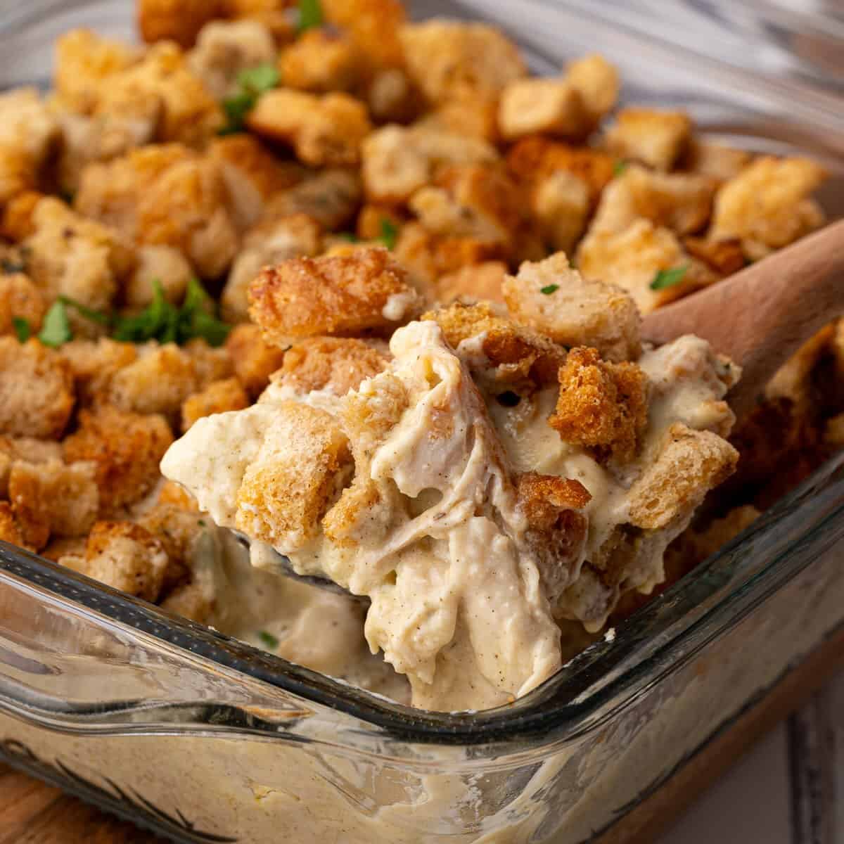 A spoonful of chicken, stuffing and gravy in a casserole dish.