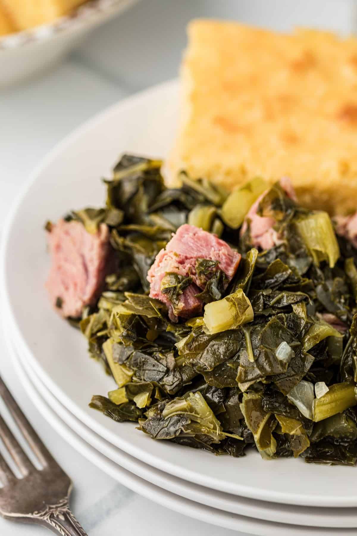 Cooked collard greens served in a bowl with cornbread on the side and pieces of ham hock mixed in.