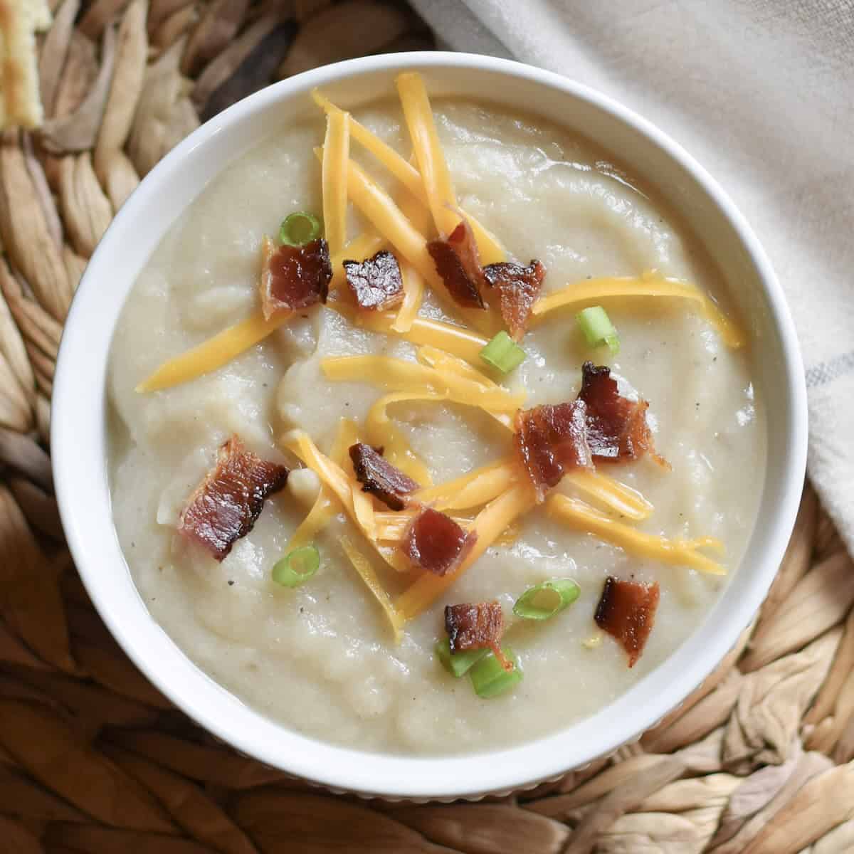 Bowl of creamy potato bacon soup topped with cheddar, crispy bacon, and green onions.