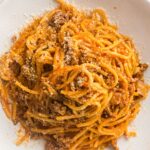 Plated spaghetti with meat sauce topped with grated Parmesan cheese.
