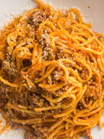 Plated spaghetti with meat sauce topped with grated Parmesan cheese.