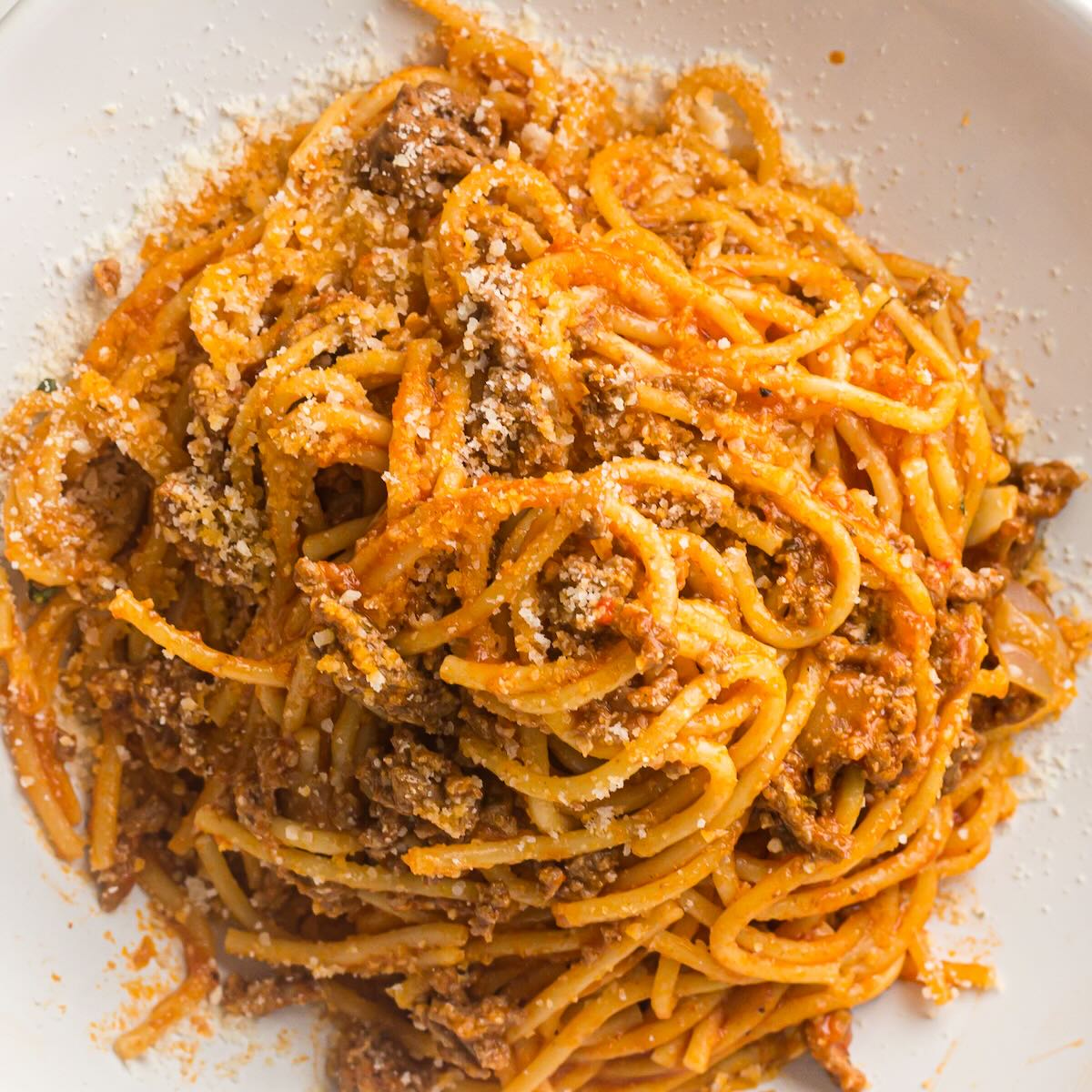 Plated spaghetti with meat sauce topped with grated Parmesan cheese.