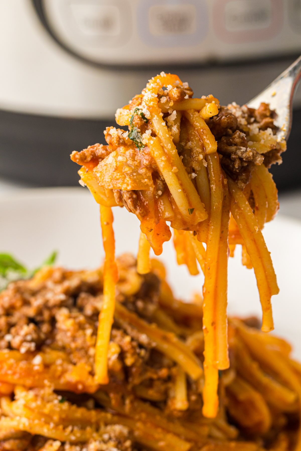 A bite full of spaghetti with meat sauce topped with grated Parmesan cheese.