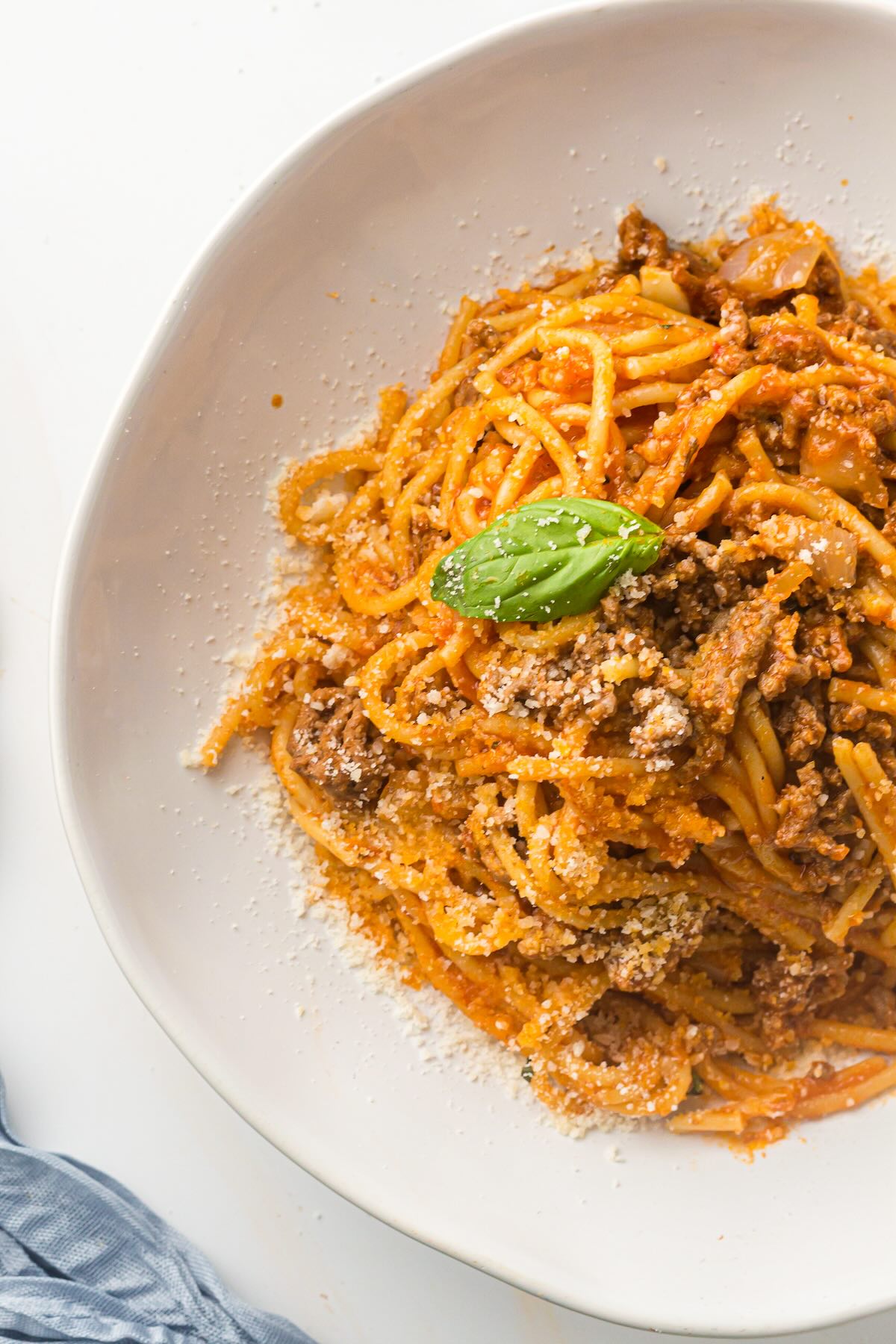 A bowl of Instant Pot spaghetti with meat sauce topped with Parmesan cheese and a basil sprig.