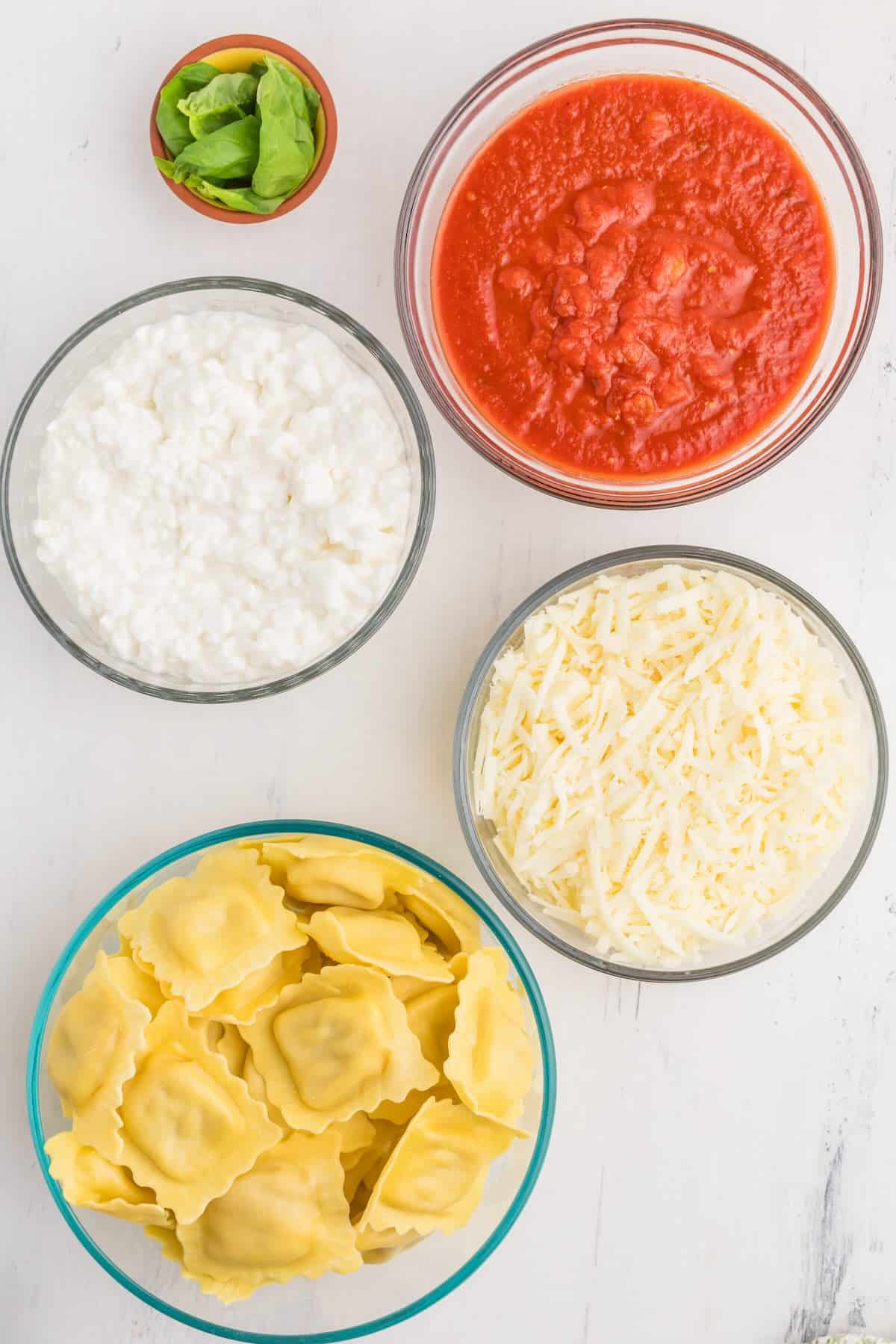 Ingredients for lazy lasagna including ravioli, pasta sauce, cottage cheese, and mozzarella.
