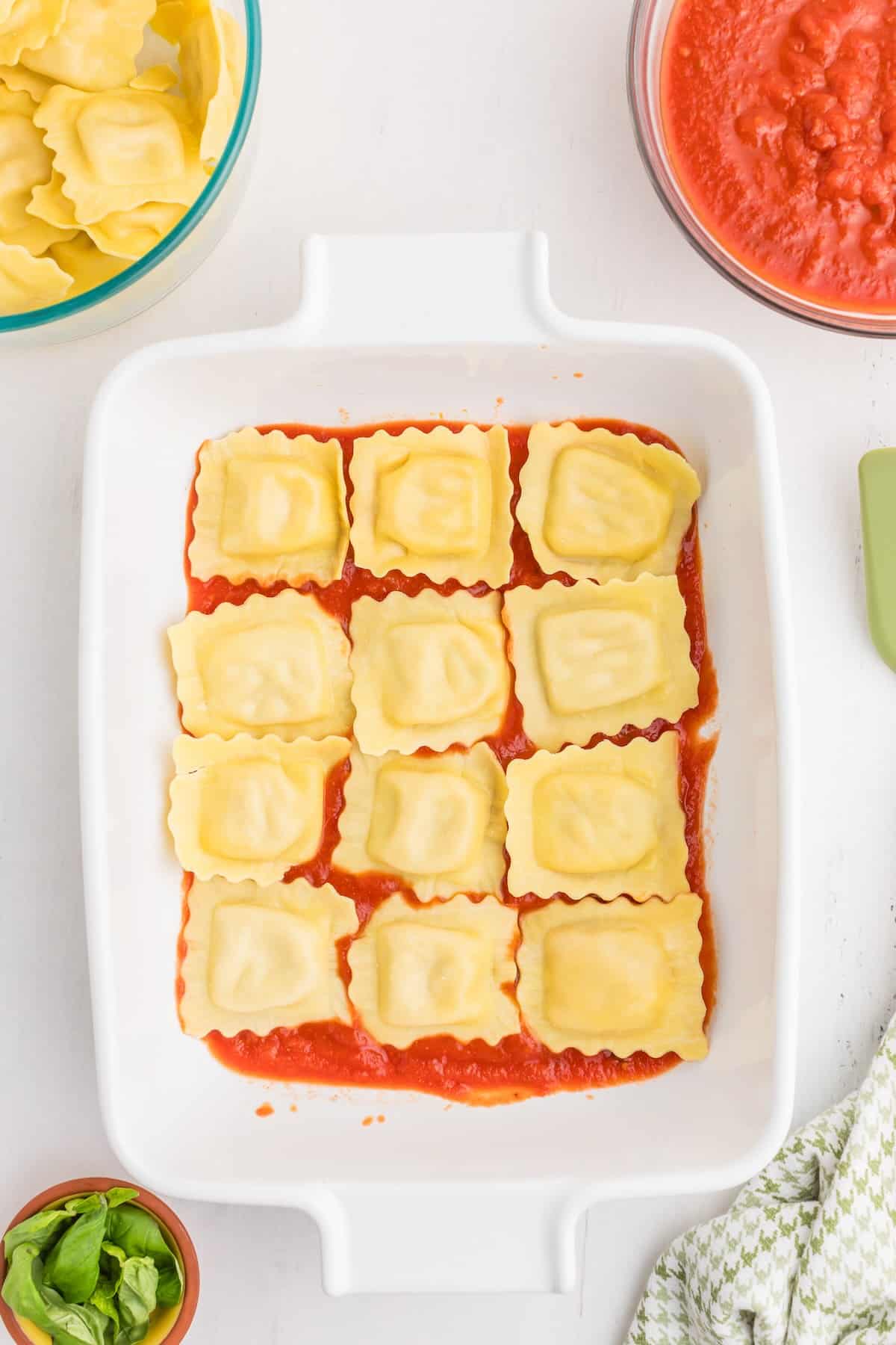 A single layer of refrigerated ravioli arranged over pasta sauce in a baking dish.