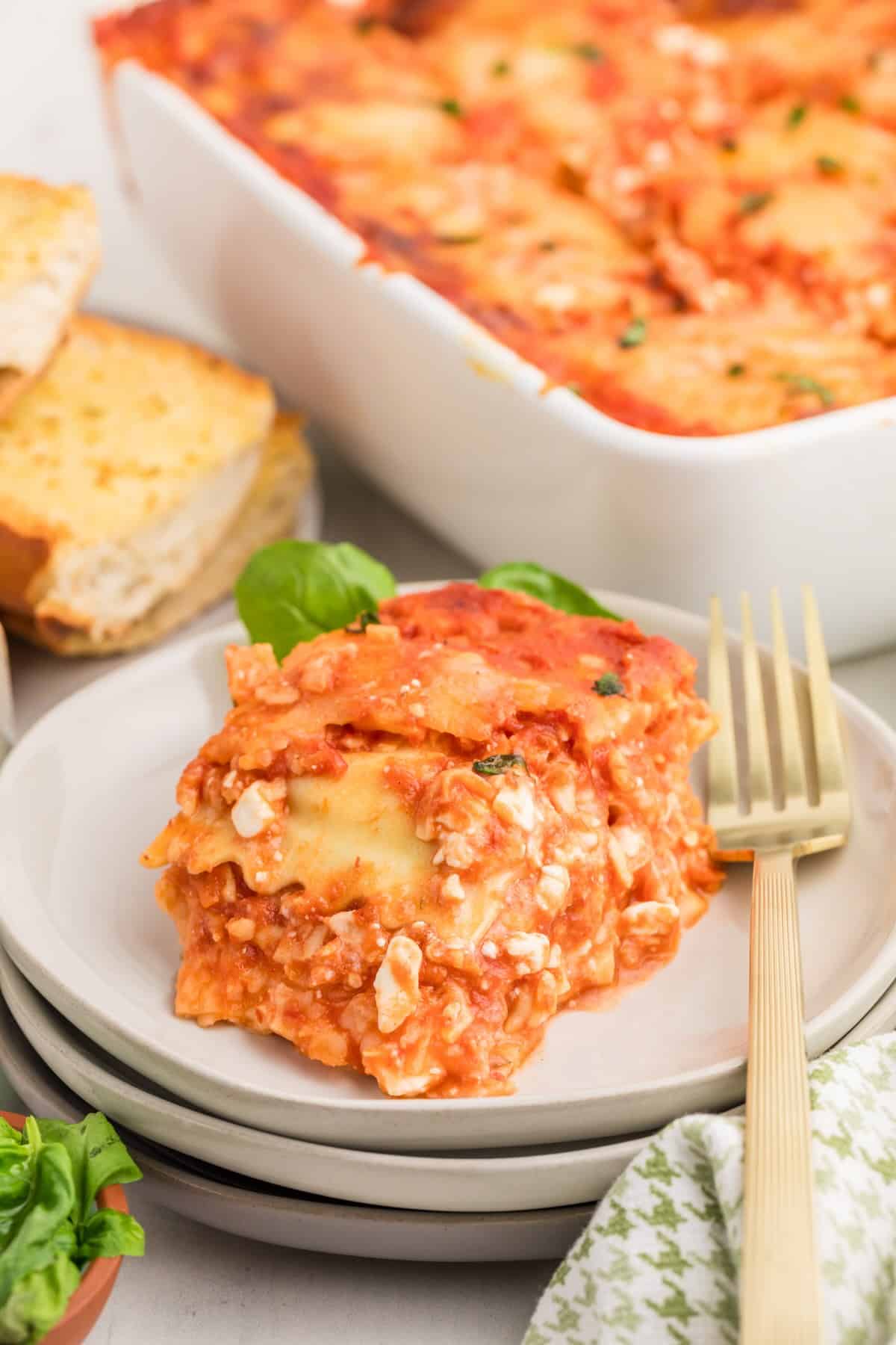 A slice of ravioli lasagna on a plate topped with fresh basil, showing the cheesy layers.