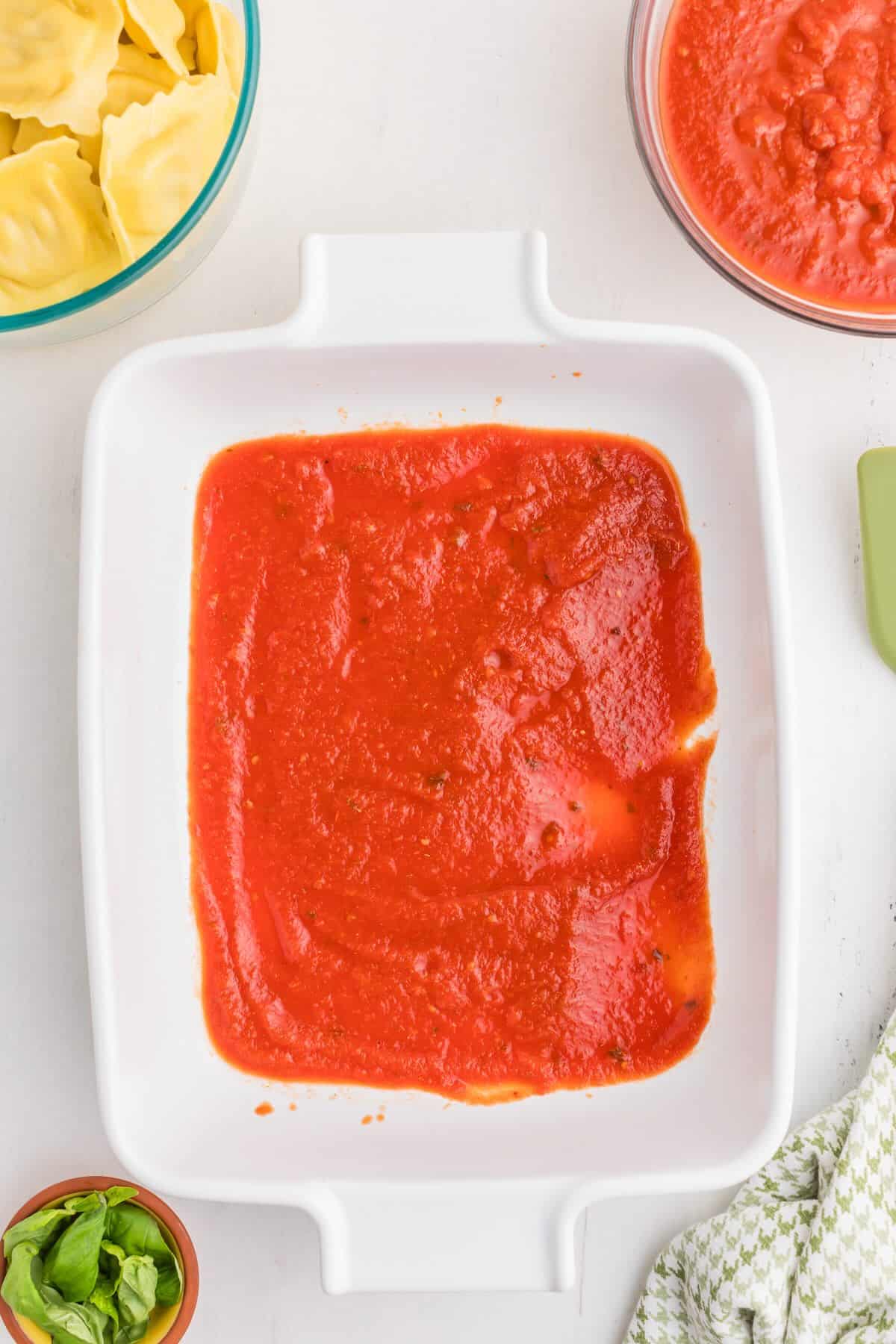 Spreading pasta sauce across the bottom of a 9×13 dish to start layering lazy lasagna.