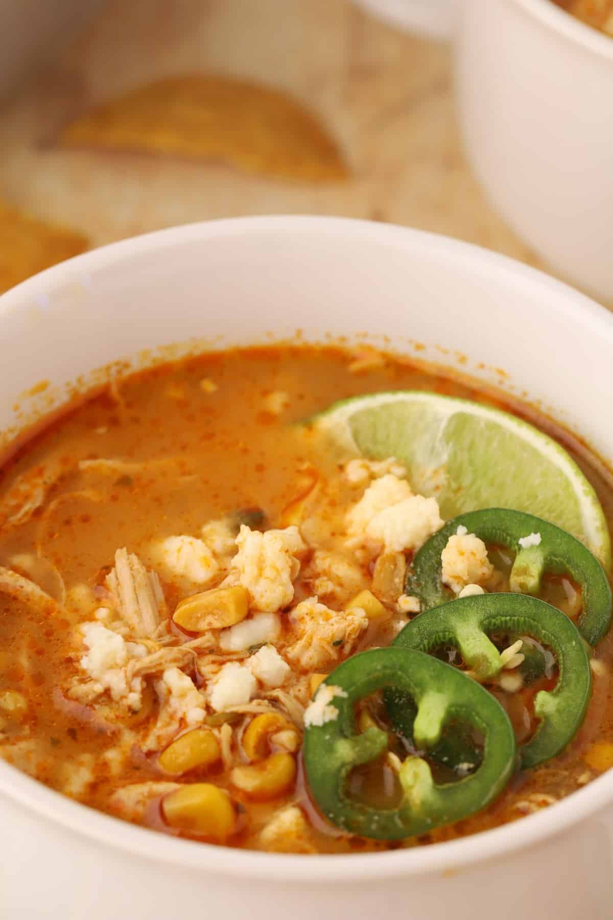 Bowl of creamy Mexican street corn soup topped with queso fresco, cilantro, and fresh lime wedges.