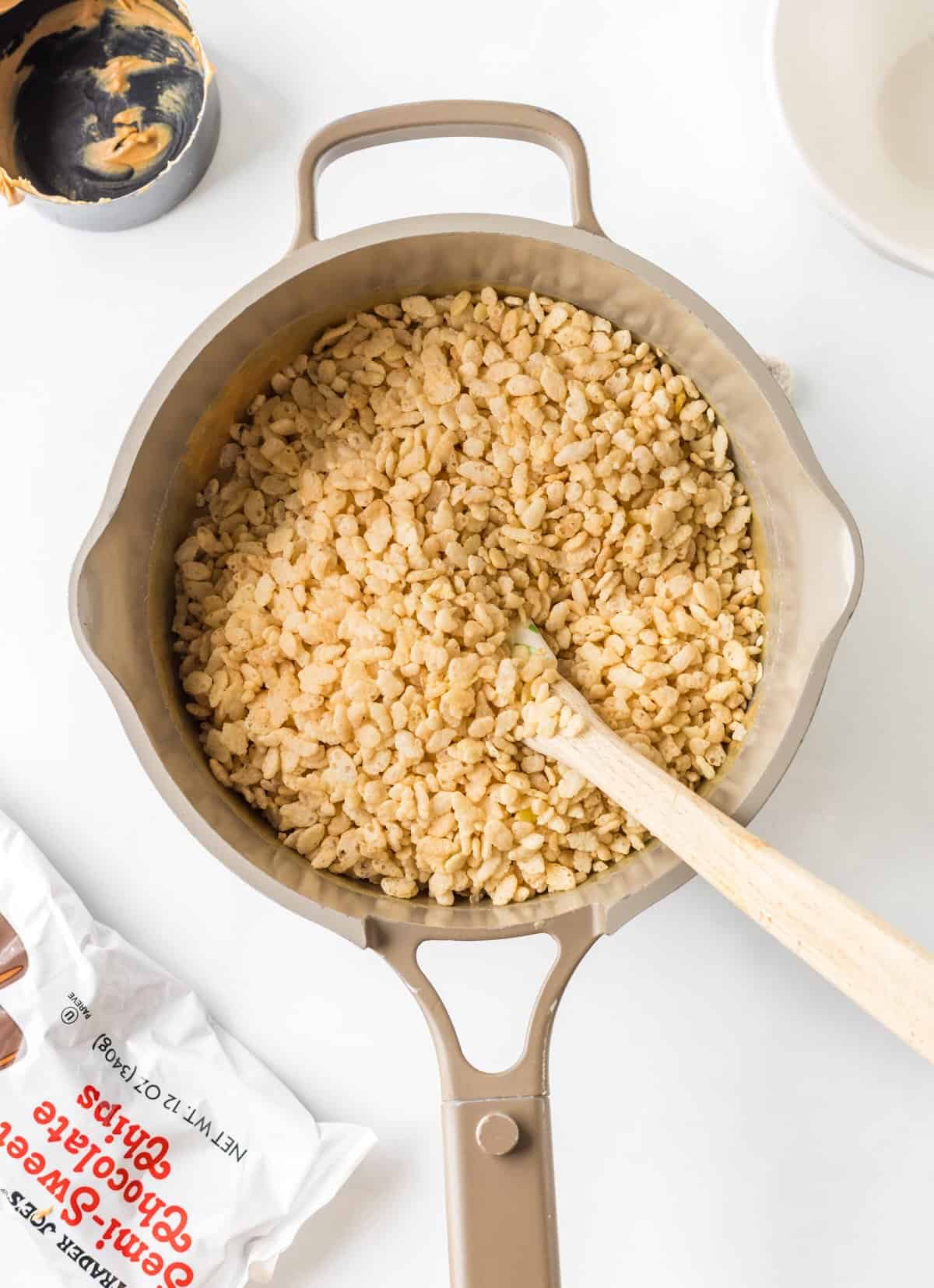 Rice Krispies cereal being stirred into peanut butter mixture for classic scotcharoo recipe.