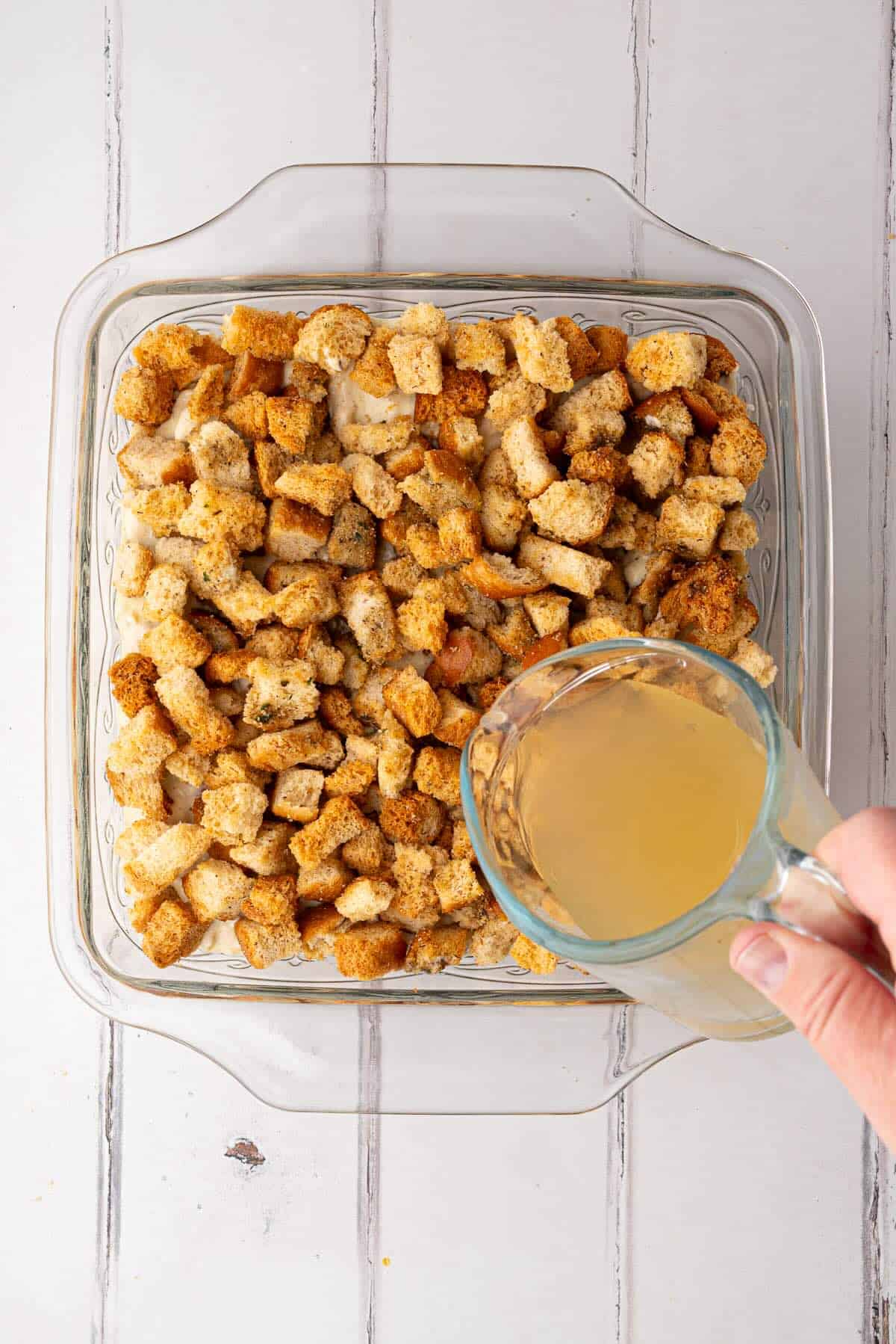 Chicken broth poured over stuffing in a baking dish.