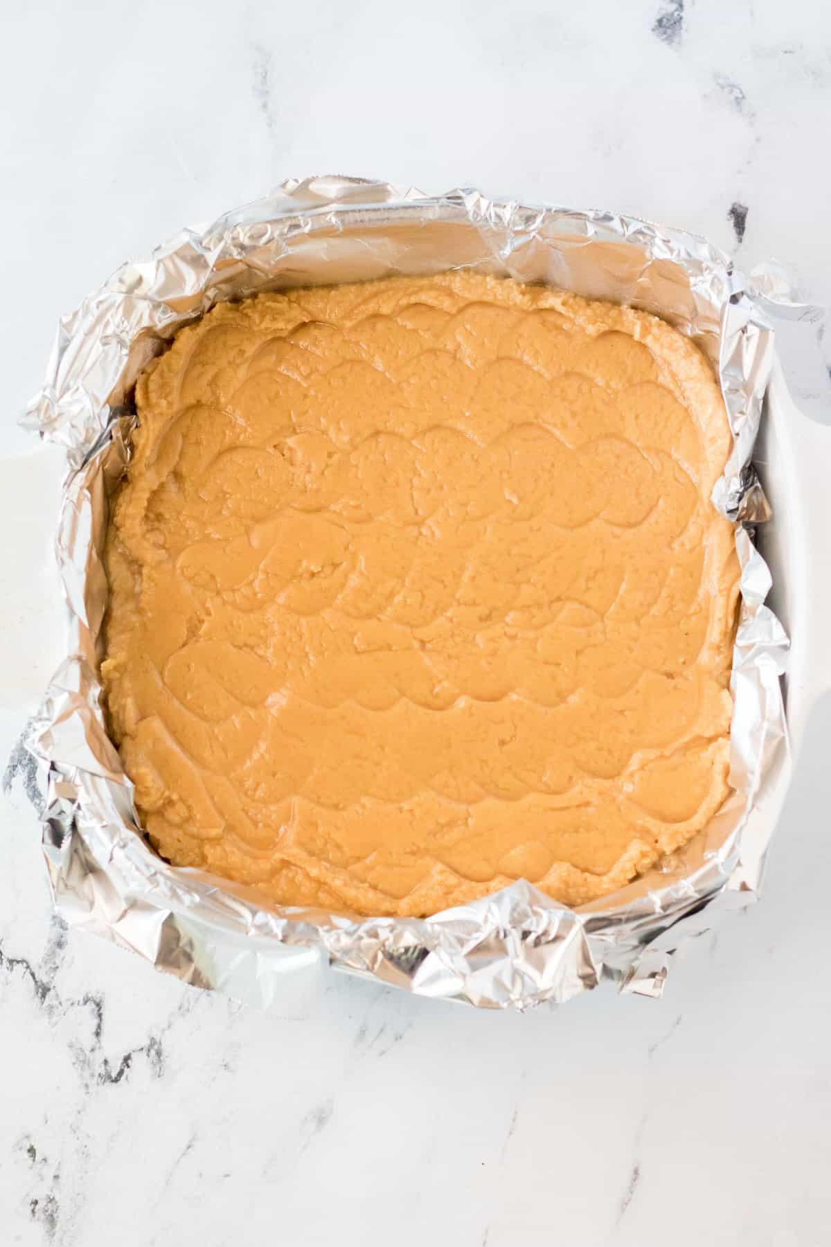 Peanut butter fudge pressed evenly into a parchment-lined baking pan before chilling.