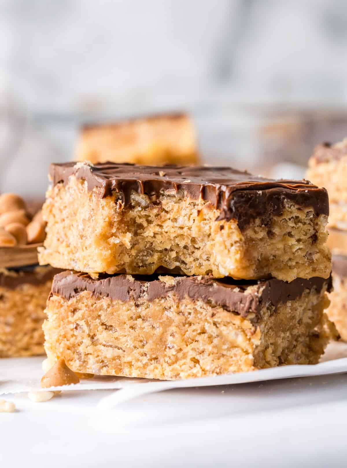 Stacked scotcharoos with a bite taken out showing the chewy texture and chocolate topping.