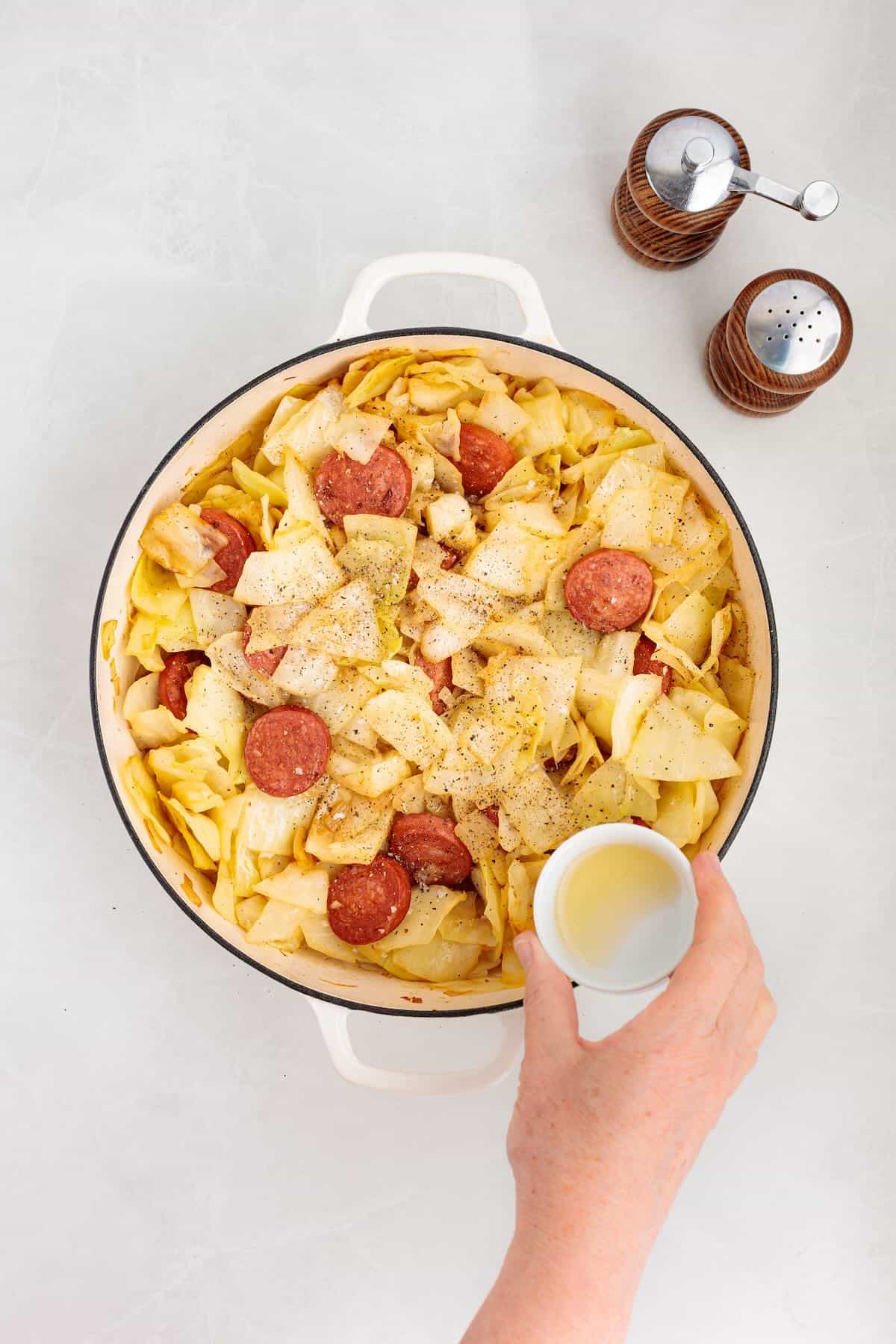 Adding apple cider vinegar, salt and pepper to kielbasa and cabbage.