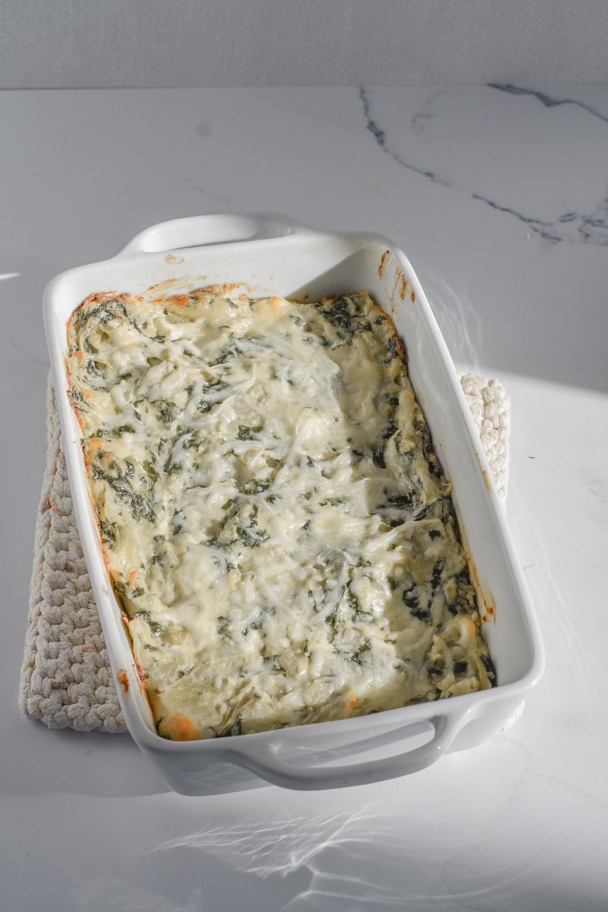 Baked spinach artichoke dip with fresh spinach and melted cheese on top.
