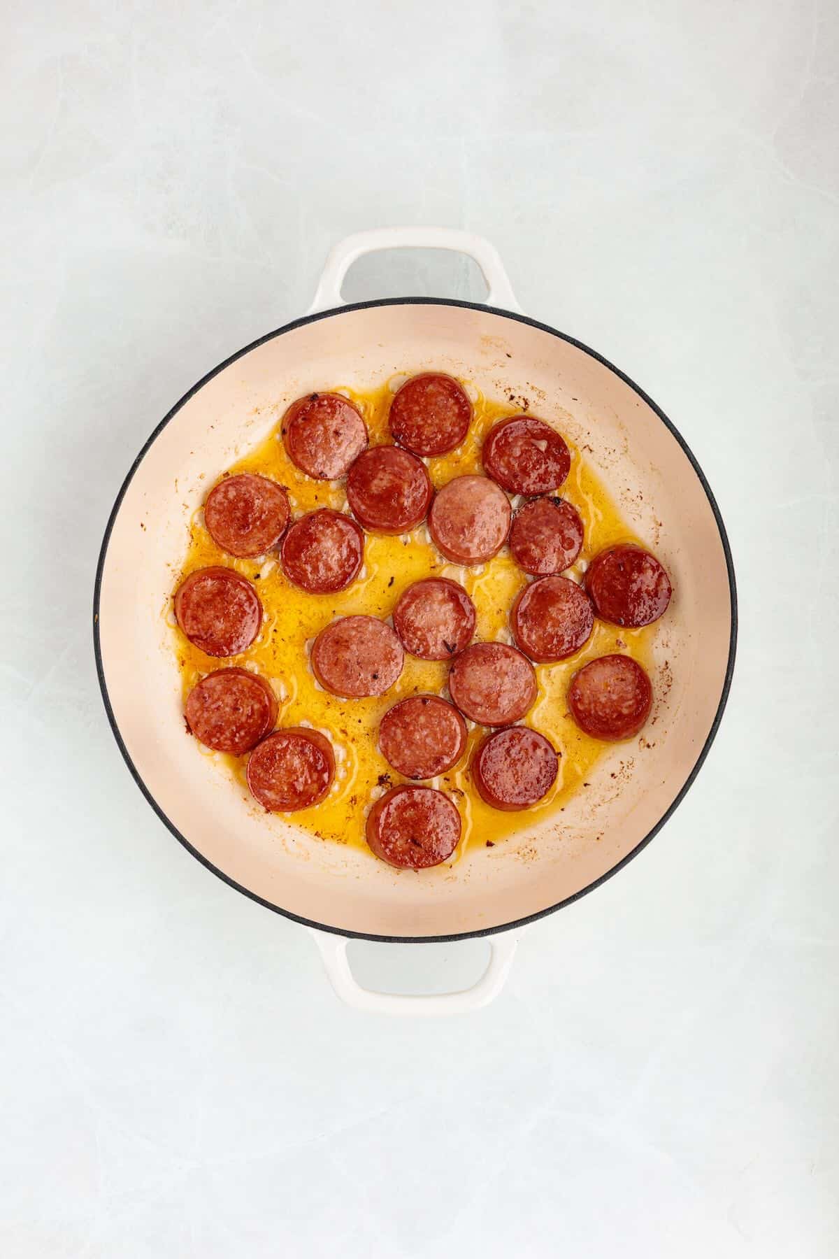 Sliced kielbasa browning in a cast iron skillet.