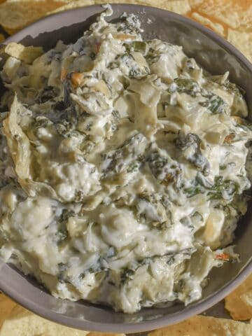 A bowl of gooey and cheesy spinach dip made with jarred artichokes and sautéed fresh spinach.
