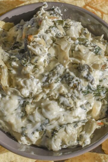 A bowl of gooey and cheesy spinach dip made with jarred artichokes and sautéed fresh spinach.