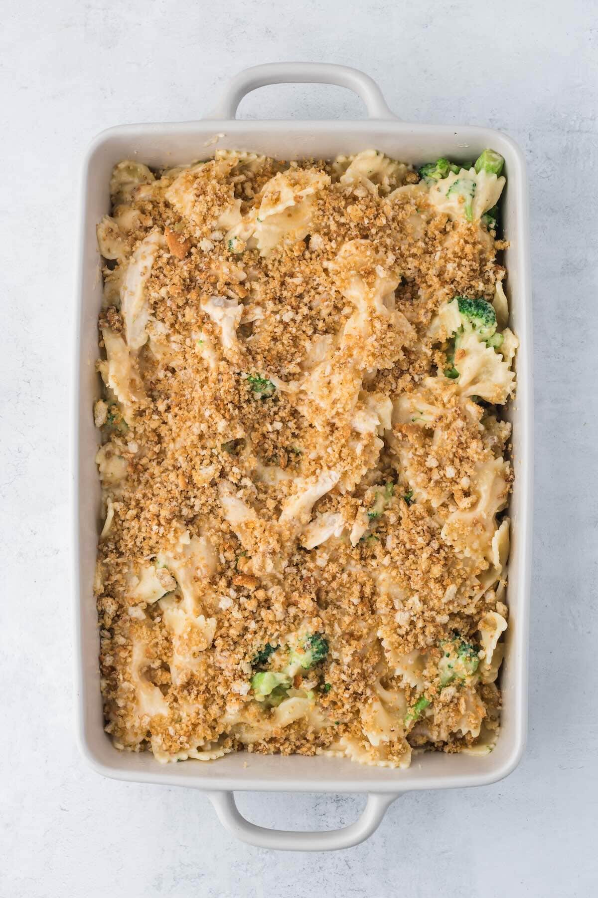 Chicken and pasta with broccoli in a casserole dish topped with breadcrumbs before baking.