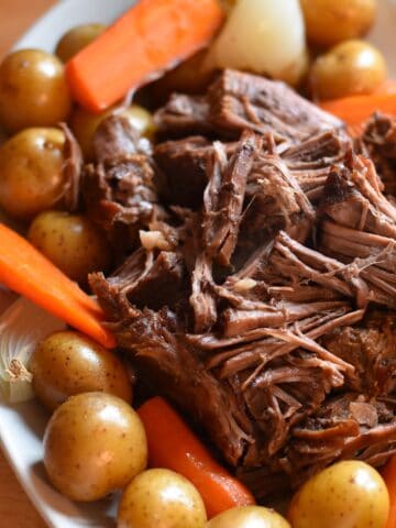 Dutch oven pot roast with tender shredded beef, carrots, potatoes, and onions.