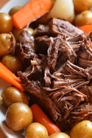 Dutch oven pot roast with tender shredded beef, carrots, potatoes, and onions.