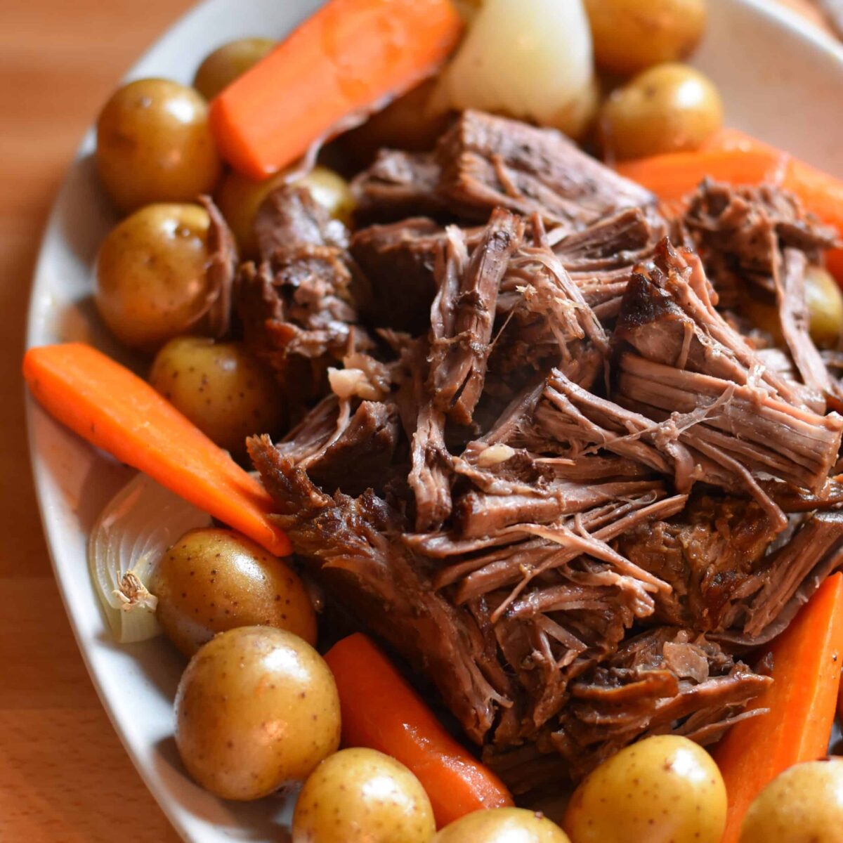 Dutch oven pot roast with tender shredded beef, carrots, potatoes, and onions.