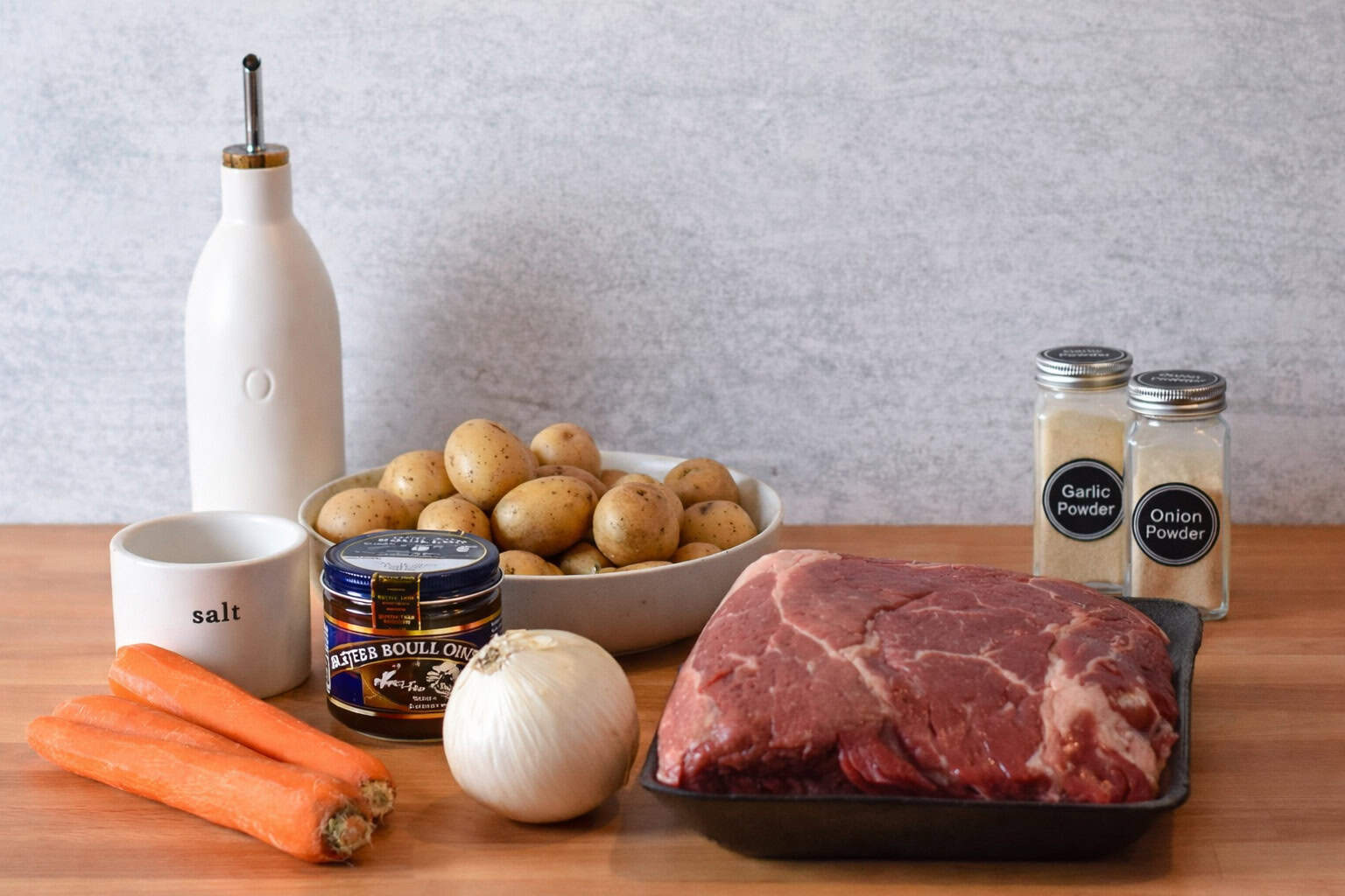 An uncooked chuck roast, carrots, onion and baby potatoes with beef broth and seasonings to make a roast in the oven.