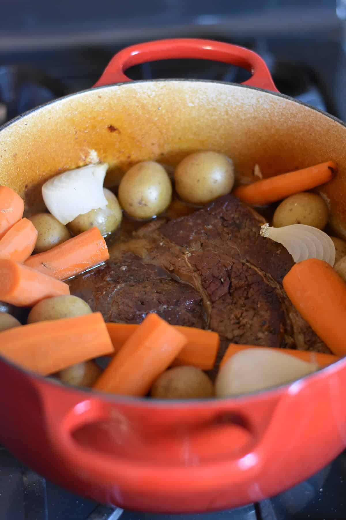A large Dutch oven filled with chuck roast, potatoes, onion wedges and carrots.