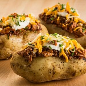 Three loaded baked potatoes with cheese, toppings, and sour cream.