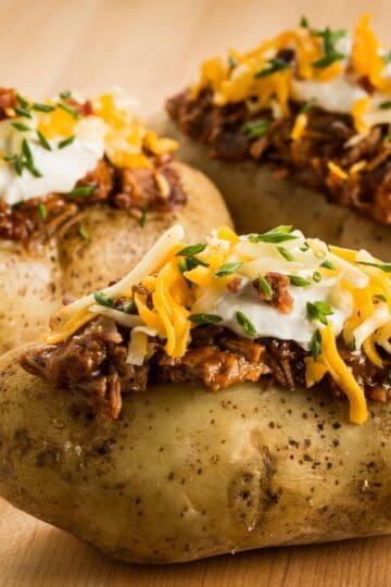 Three loaded baked potatoes with cheese, toppings, and sour cream.