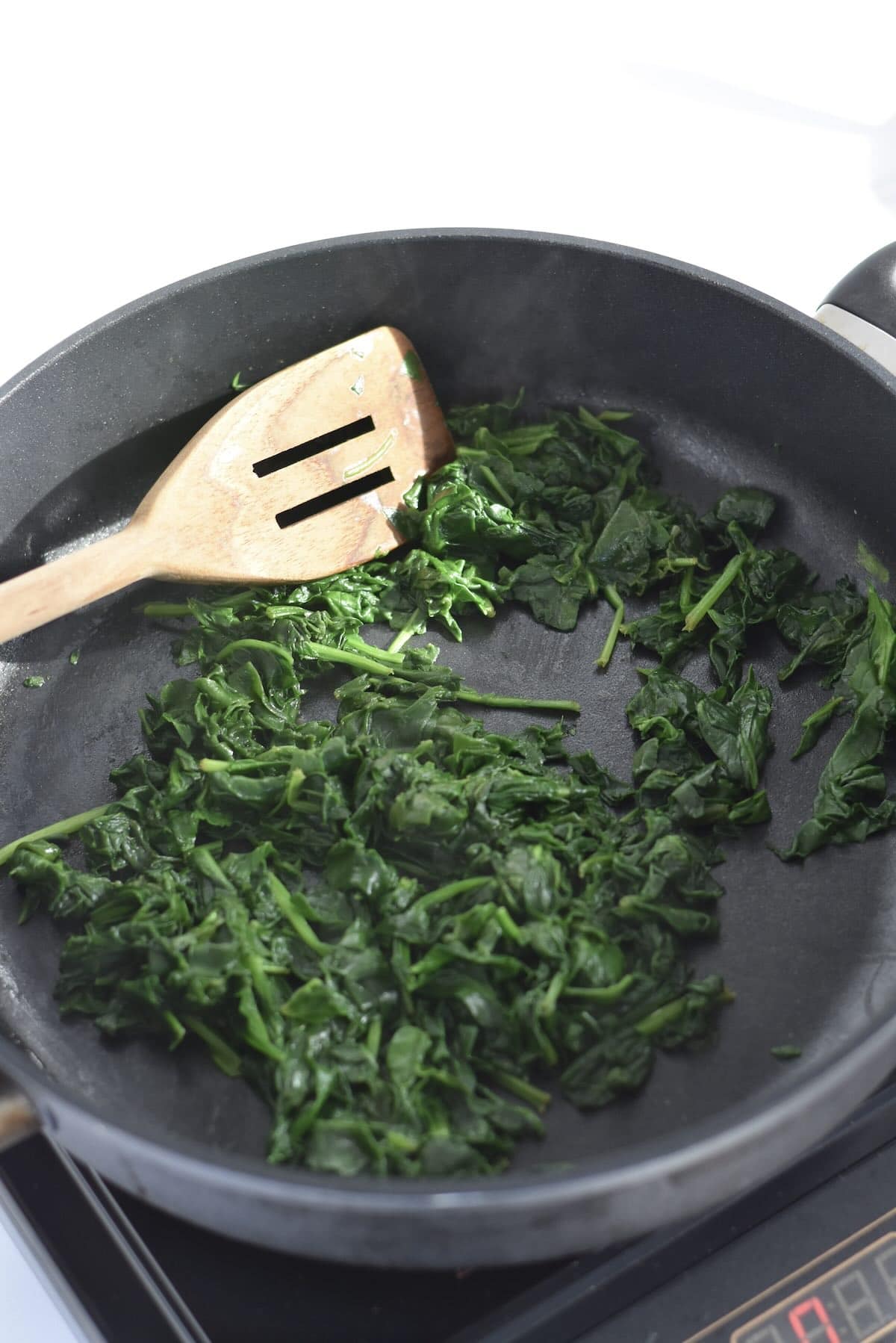 Fresh spinach wilting in a skillet for spinach artichoke dip.