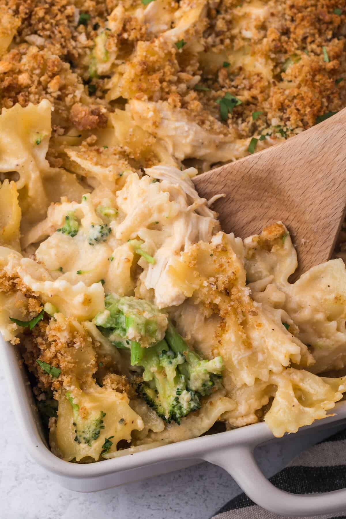A wooden spoon serving up warm and hearty baked pasta, chicken and broccoli.