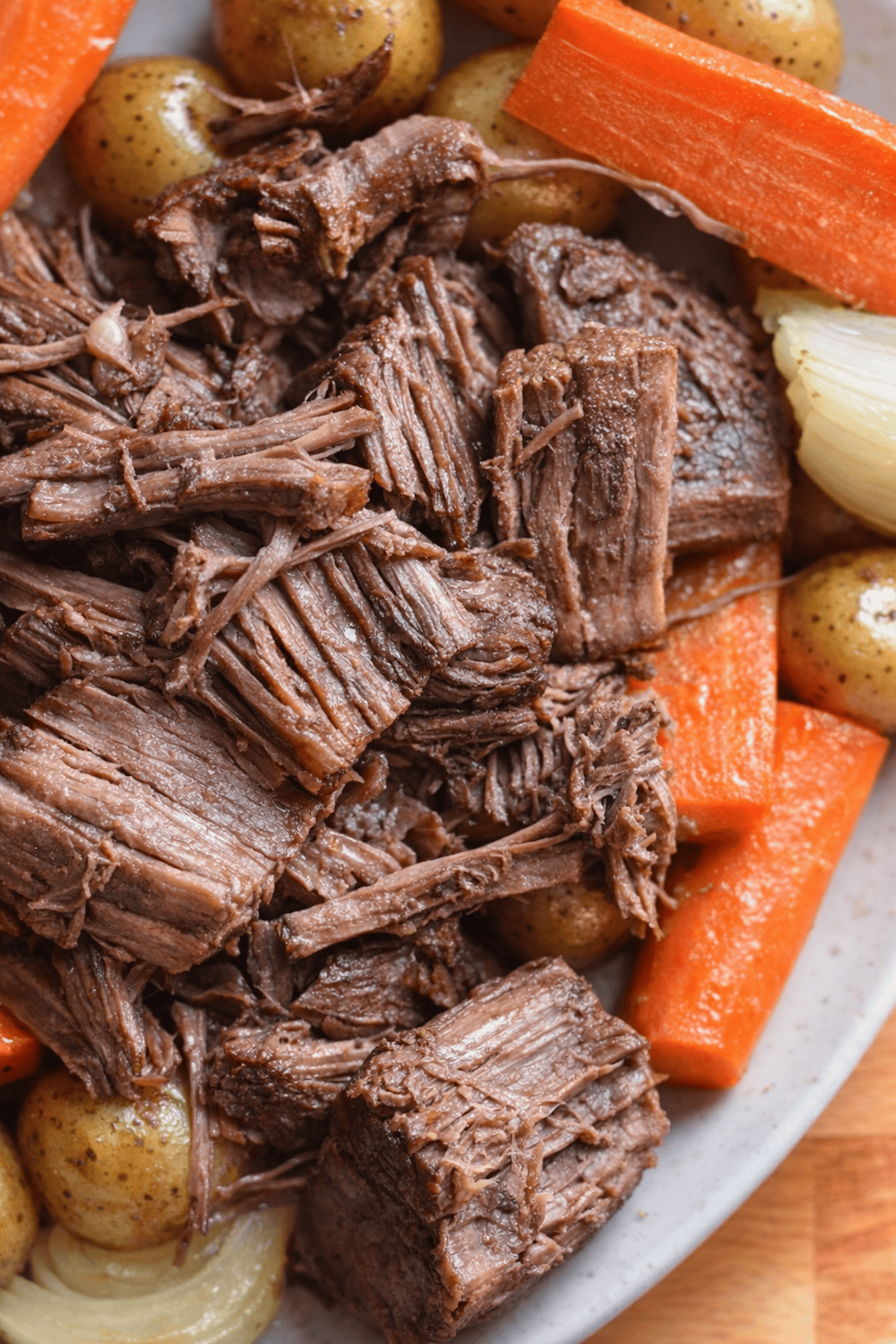 Tender shredded beef on a platter with carrots, potatoes and onions.