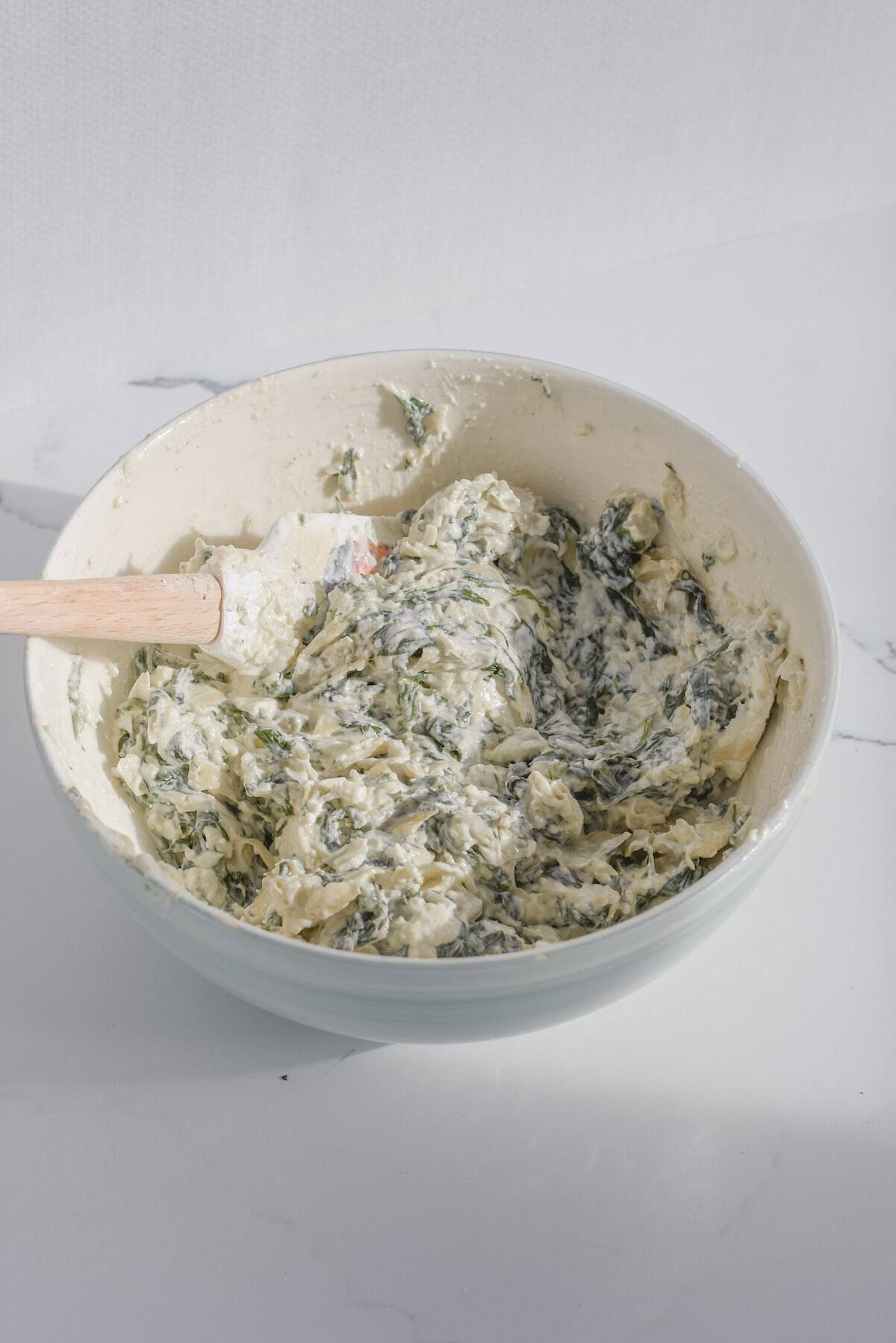 Spinach artichoke dip mixed with fresh spinach and cheese before baking.