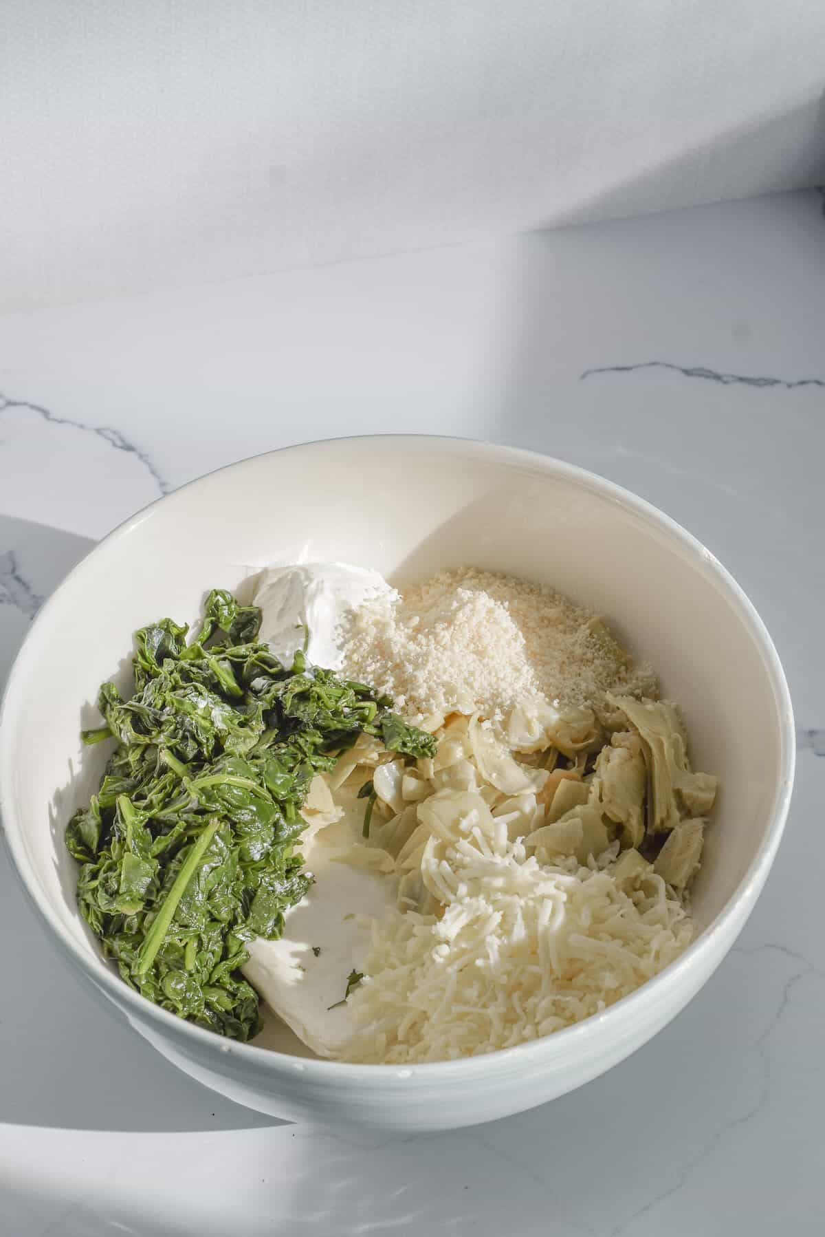Spinach, cream cheese, cheese and artichoke hearts mixed in a bowl.