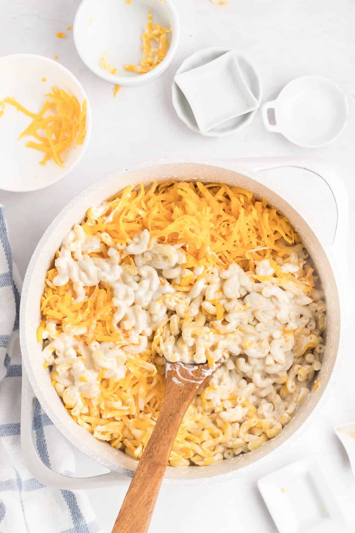 Shredded cheese being stirred into pasta off heat to make smooth stovetop mac and cheese sauce.